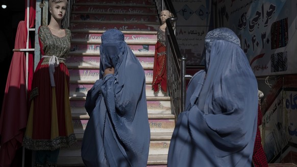 Burka-wearing Afghan women walk past a clothing shop, in Herat, Afghanistan, Tuesday, Nov. 23, 2021. (AP Photo/Petros Giannakouris)