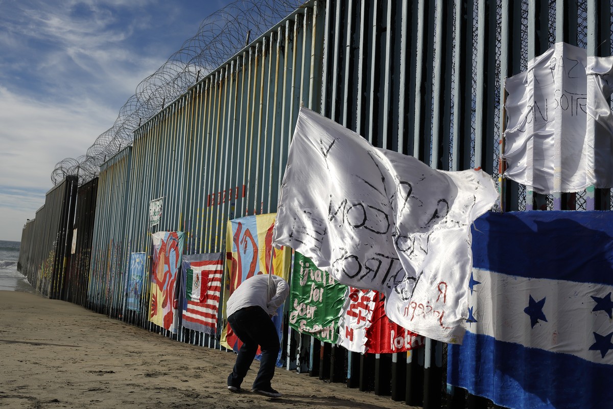 Joseph, an migrant from Honduras, plants a white flag with the words, "peace and God with us," in front of the border wall during an art display on the border wall, topped with razor wire, T ...