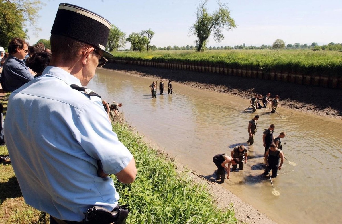 A gendarme, left, looks at French soldiers searching for art objects in a canal in Gerstheim, eastern France , Thursday May 16, 2002. Investigators partly emptied the canal between the Rhone and the R ...