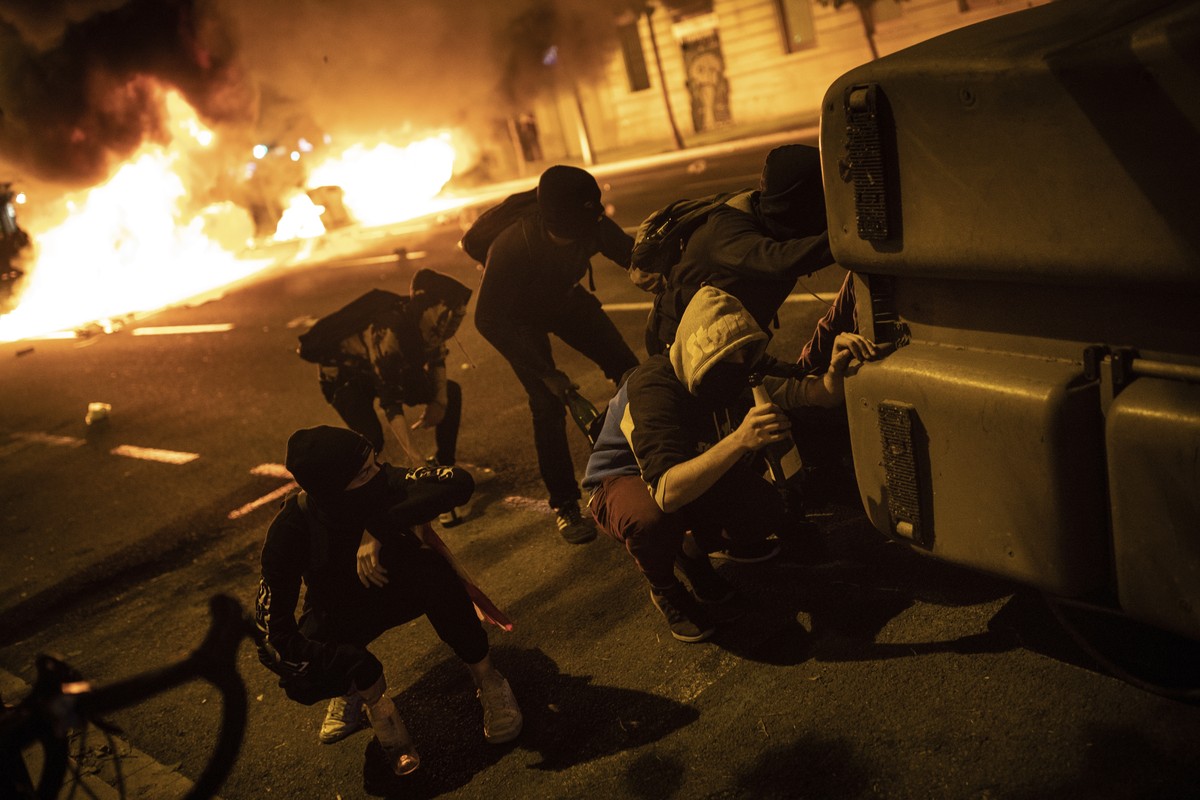 Protestors take shelter behind a barricade during clashes with police in Barcelona, Spain, Wednesday, Oct. 16, 2019. Spain's government said Wednesday it would do whatever it takes to stamp out v ...