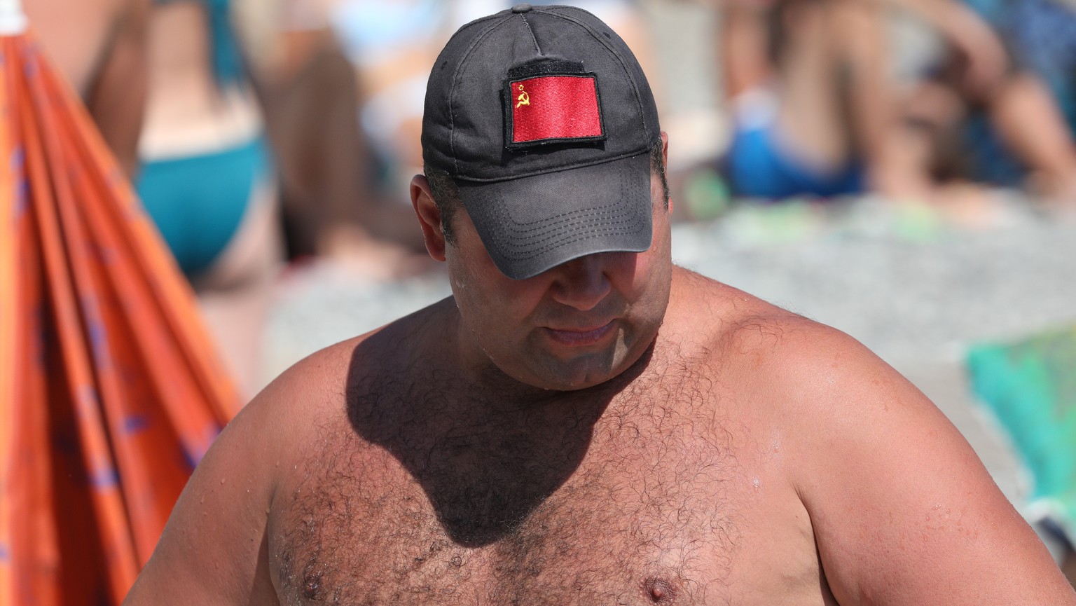 epa10778096 A man wearing a cap and a red flag of the former Soviet Union rests on a beach on the Black Sea in Alushta, Crimea, July 24, 2023 (issued July 31, 2023).  Crimea was annexed by Russia in 2014, shortly after...