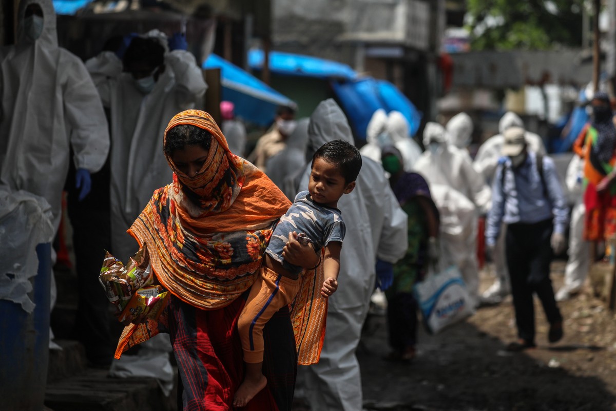 epa08538584 A woman carrying a toddler walks pass as the health workers wearing personal protective equipment (PPE) arrive to carry a medical checkup to the residents of a 'containment zones' ...