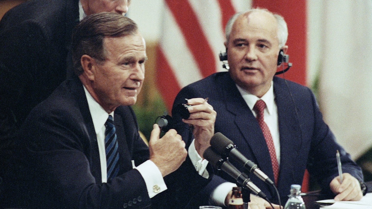 FILE In this file photo taken on Sunday, Sept. 9, 1990, U.S. President George H. Bush works to get an earphone plug from his ear as Soviet President Mikhail Gorbachev laughs during their joint news co ...