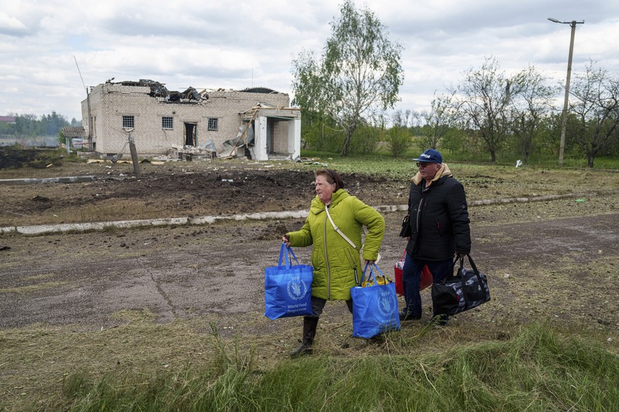 People walk with their belongings to the evacuation point in front of a building that was damaged by a Russian airstrike in Vilcha, near Vovchansk, Ukraine, Sunday, May 12, 2024. (AP Photo/Evgeniy Mal ...