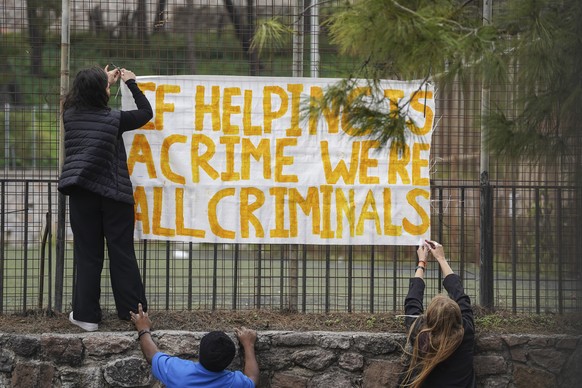 Supporters of the 24 aid workers and volunteers of 24 aid workers and volunteers accused of participating in migrant rescue operations hang up a banner outside the court in Mytilene, on the northeaste ...