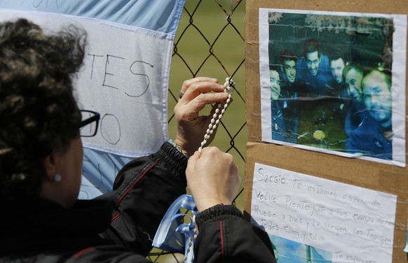 A woman wraps a rosary on the link of a fence blanketed with national flags in support of the crew members of the lost submarine, on the perimeters of the naval base in Mar del Plata, Argentina, Tuesd ...