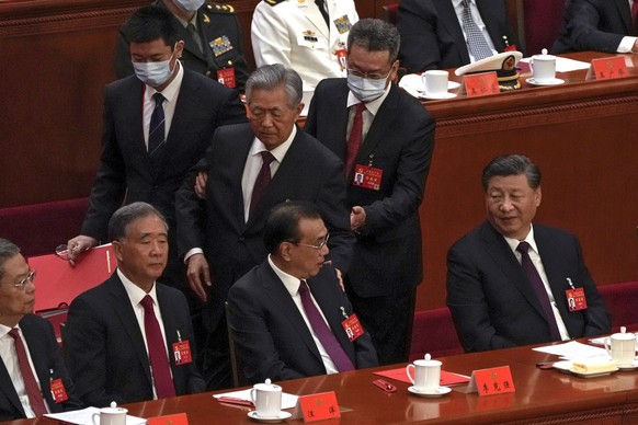 Chinese President Xi Jinping, right, looks on as former Chinese President Hu Jintao, standing at center, touches the shoulder of Premier Li Keqiang, center, as he is assisted to leave the hall during  ...