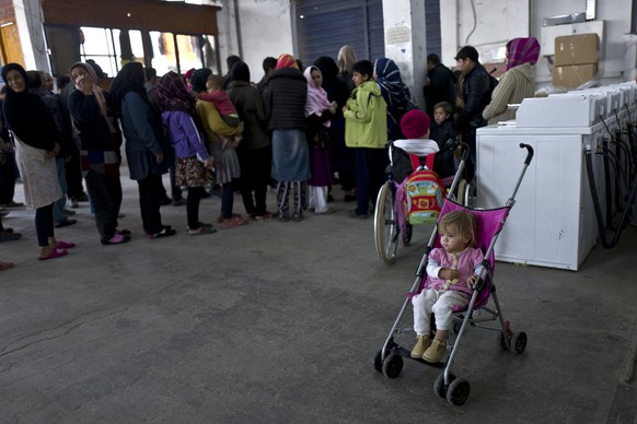 An Afghan refugee child waits for her father in a stroller while he and others line up to receive winter coats at the refugee camp of Oinofyta about 58 kilometers (36 miles) north of Athens, Thursday, ...