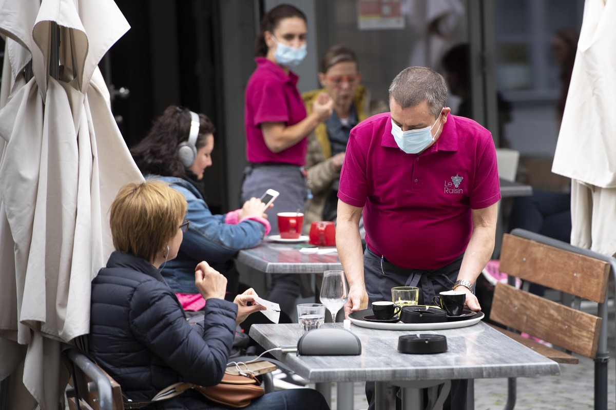 A waiter wearing protective face mask of "Le Raisin" cafe restaurant brings drinks to customers in a terrace the day of its reopening during the state of emergency of the coronavirus disease ...