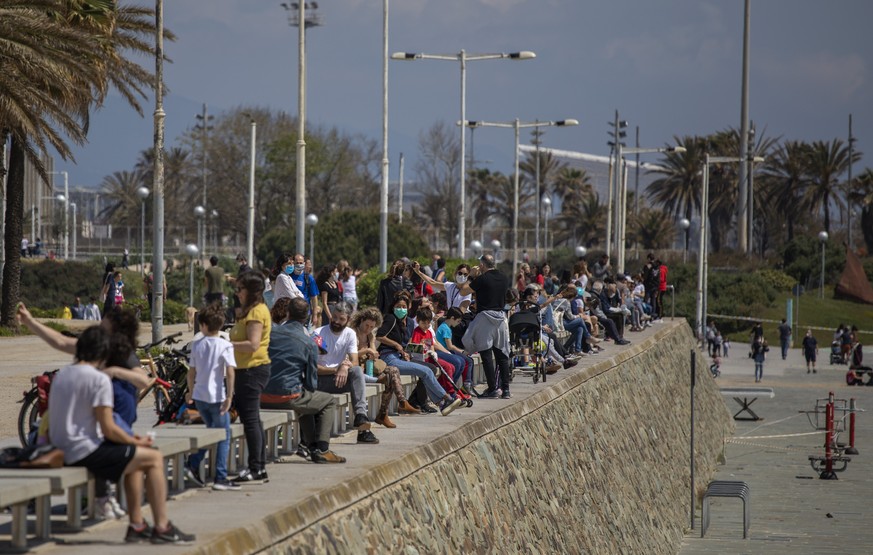 Families with their children sit in a boulevard as police patrol the beach, where access is prohibited, in Barcelona, Spain, Sunday, April 26, 2020 as the lockdown to combat the spread of coronavirus  ...