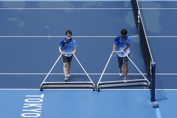 Volunteers work to dry a tennis court before the start of the tennis matches at the 2020 Summer Olympics, Tuesday, July 27, 2021, in Tokyo, Japan. (AP Photo/Seth Wenig)