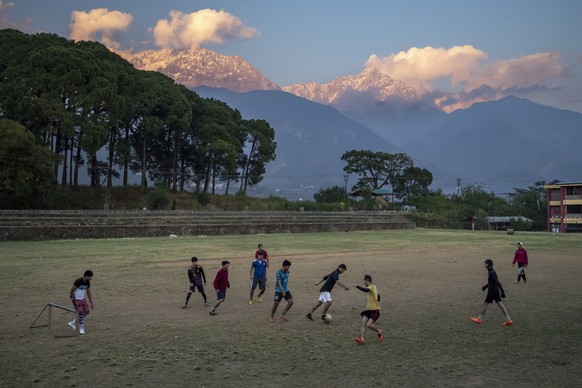 Young men play soccer at a playground against the backdrop of the Dhauladhar range of the Himalayas in Dharamshala, India, Friday, Nov. 11, 2022. (AP Photo/Ashwini Bhatia)