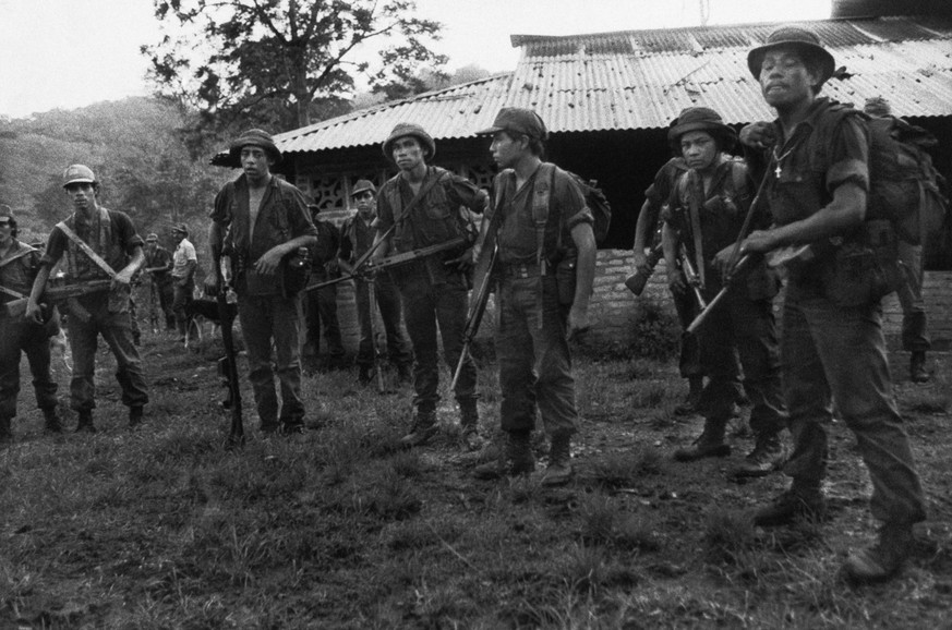 &quot;Contra&quot; troops assemble at Pinta De Maria after their raid on nearby Santa Rose de Cua in the mountains of Nicaragua, June 24, 1985. The soldier at far right, with crucifix , is the leader  ...