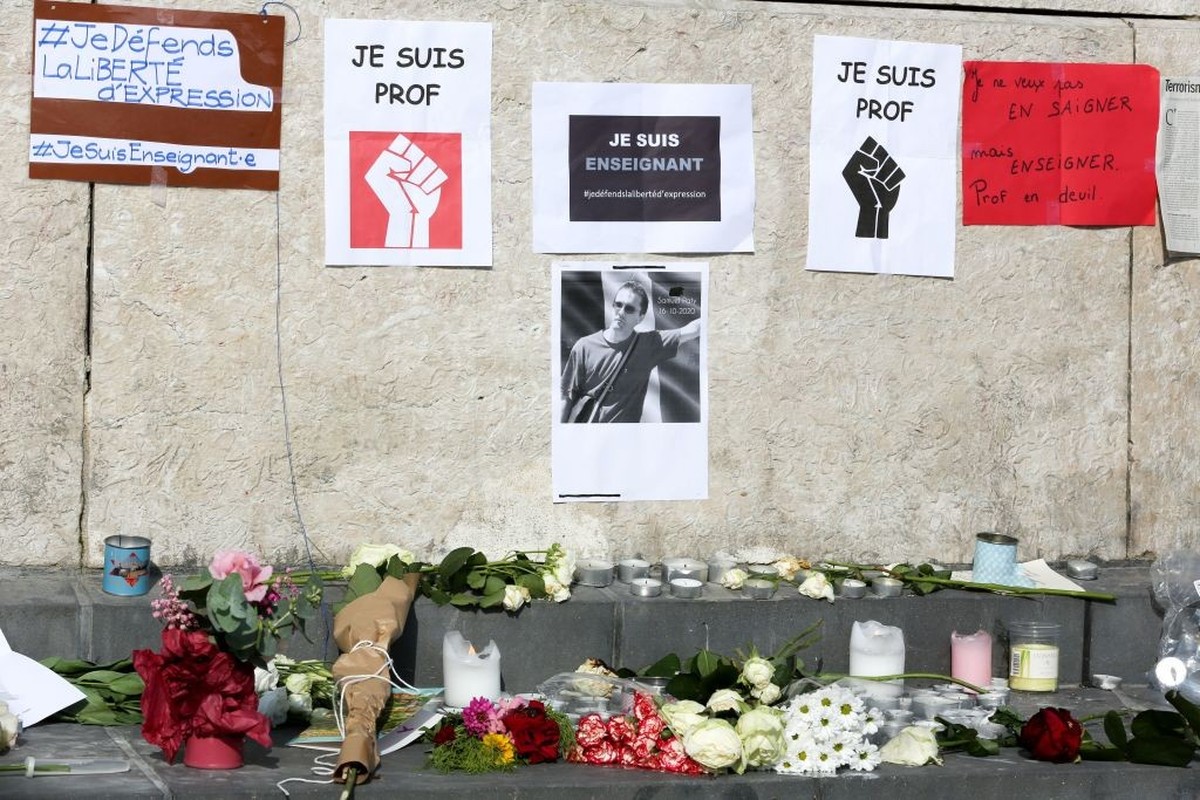 Flowers are placed in front of the portrait of history teacher Samuel Paty as people gather on Place de la Republique in Paris on October 18, 2020, two days after he was beheaded by an attacker who wa ...