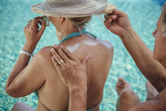 ältere Dame wird am Rücken mit Sonnencreme eingecremt