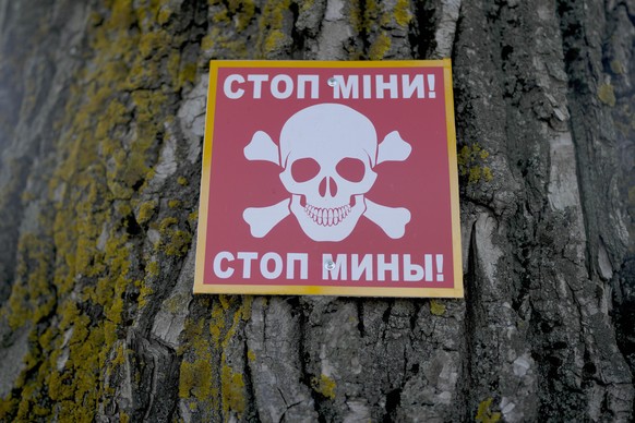 A notice warning about land mines is attached to a tree near where Ukrainian specialized team searches for mines in a field in the outskirts of Kyiv, Ukraine, Thursday, June 9, 2022. (AP Photo/Natacha ...