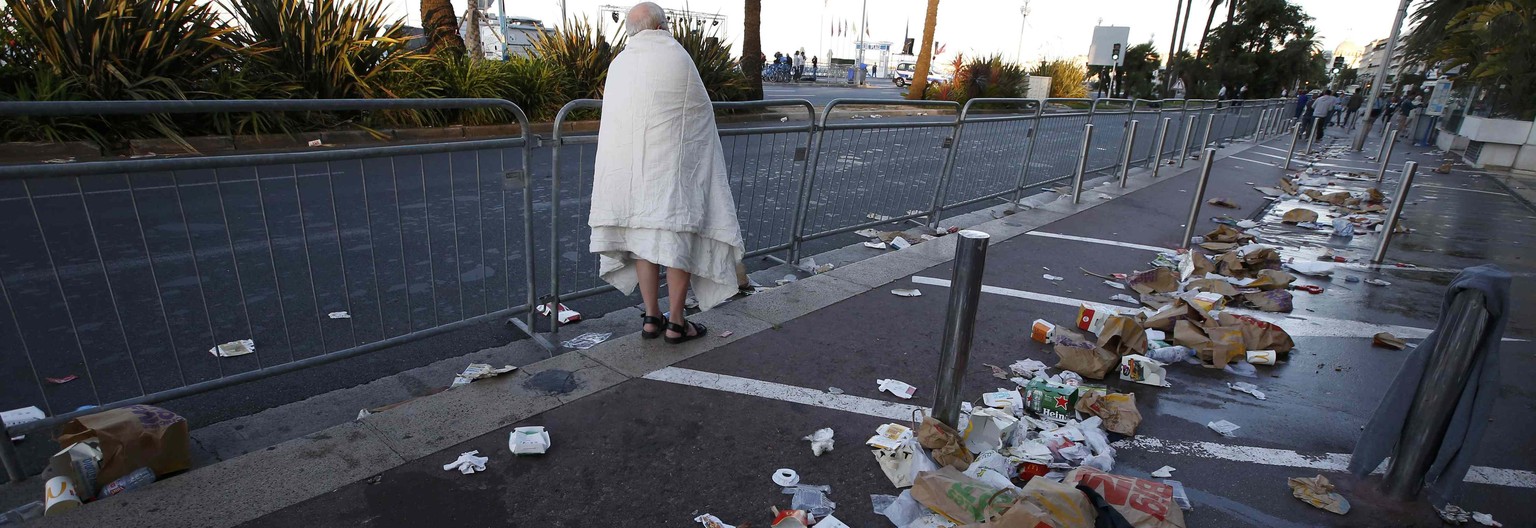 A man walks through debris scatterd on the street the day after a truck ran into a crowd at high speed killing scores celebrating the Bastille Day July 14 national holiday on the Promenade des Anglais ...