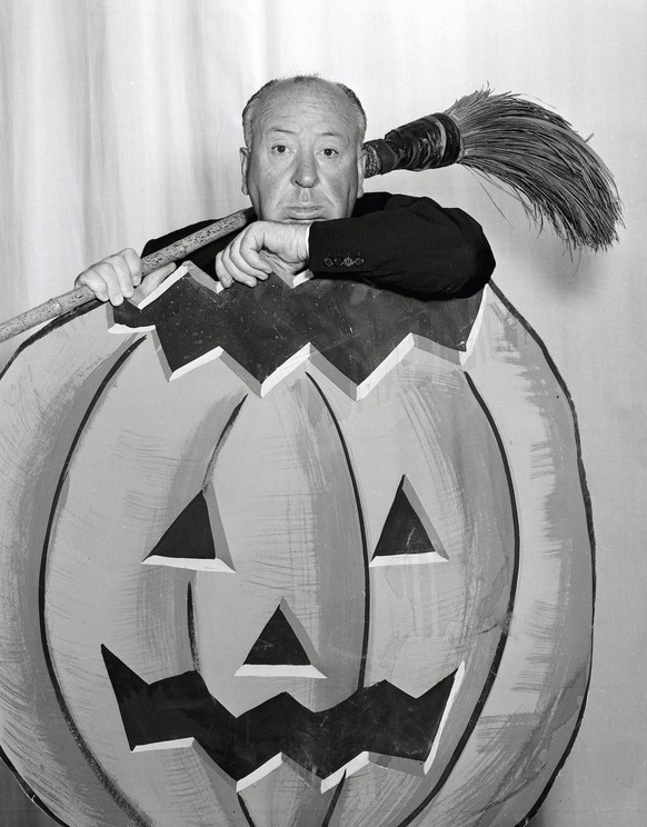 Publicity photo of Film and television director Alfred Hitchcock holds a broom and poses behind a painted Halloween pumpkin, for his anthology television series Alfred Hitchcock Presents, 1958 CBS Fil ...