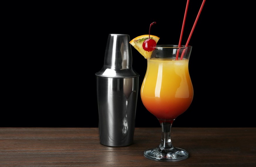 Glass of Sex on the Beach cocktail and shaker against a dark background