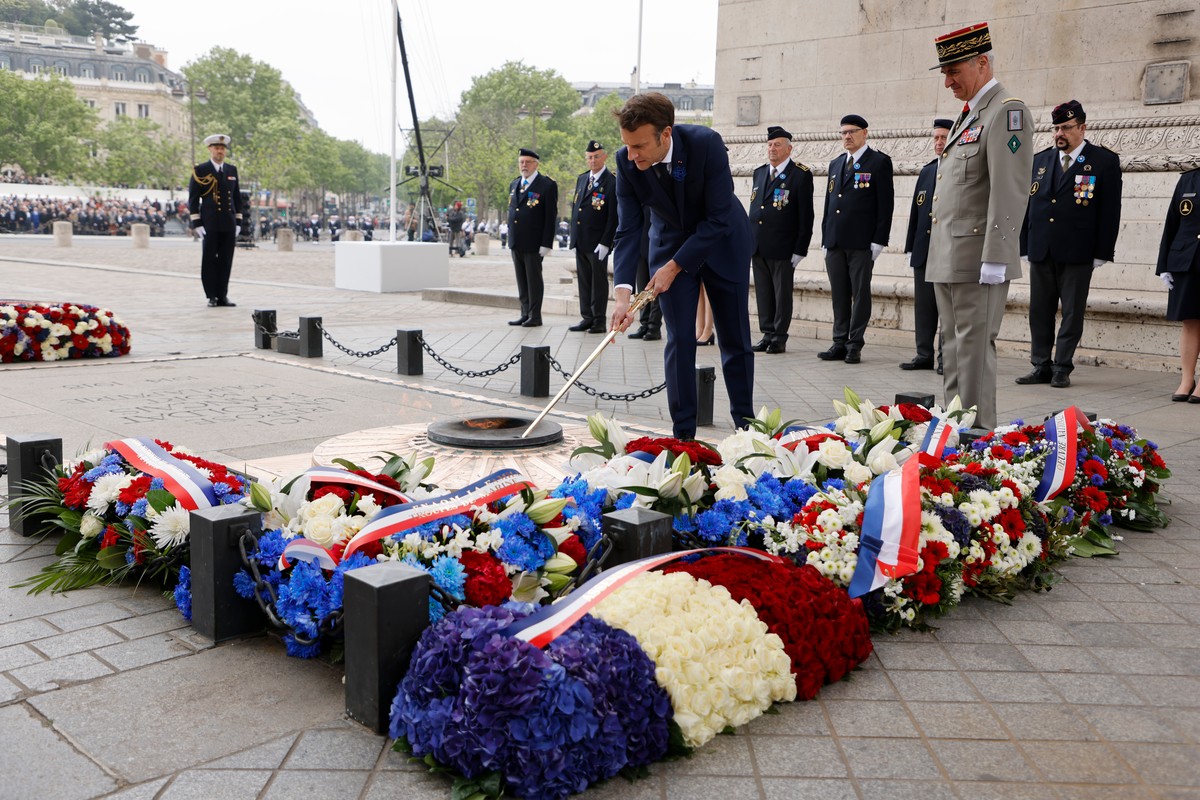 epa09933307 France's President Emmanuel Macron (C) lights the flame on the tomb of the unknown soldier at the Arc de Triomphe during the ceremonies marking the Allied victory against Nazi Germany ...