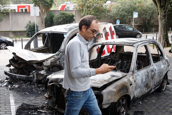 epa11684587 A man passes in front of burned vehicles after they were set on fire in the Benfica neighborhood of Lisbon, Portugal, 26 October 2024. Thirteen light vehicles and five motorcycles were set ...