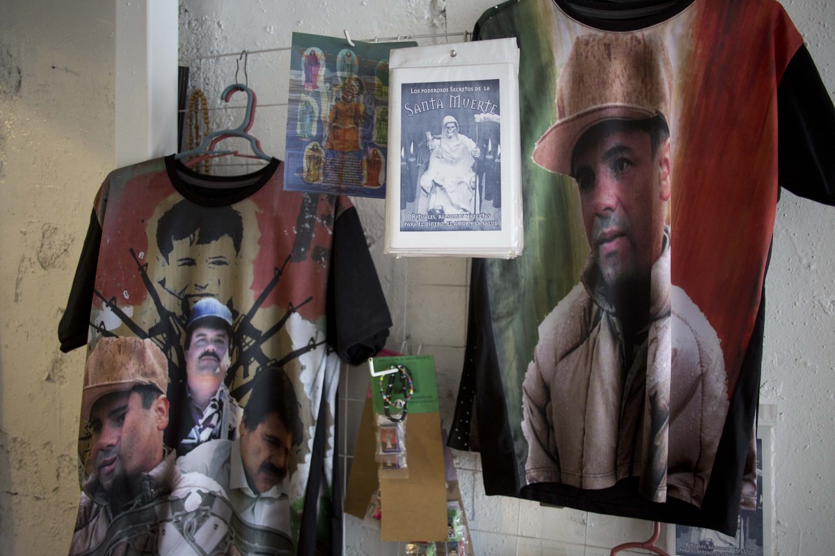 FILE - T-shirts emblazoned with images of Mexican drug lord Joaquin "El Chapo" Guzman hang for sale inside the shrine of a faith healer, in Mexico City, Oct. 16, 2015. (AP Photo/Eduardo Verd ...