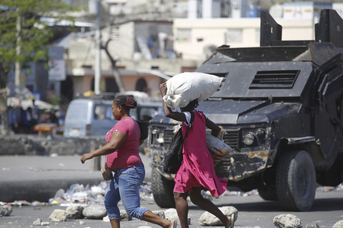 FILE - Pedestrians run past an armored police car in Port-au-Prince, Haiti, Thursday, March 7, 2024. Unrelenting gang attacks in Haiti have paralyzed the country and left it with dwindling supplies of ...