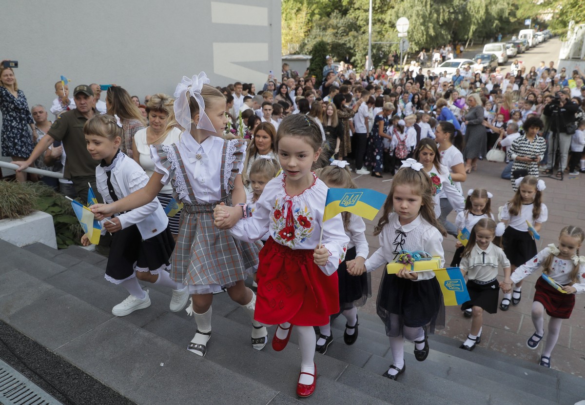 epa10151904 Children wave Ukraine's national flags as they arrive for the start of the new school year, known as 'Day of Knowledge', in Kyiv, Ukraine, 01 September 2022. In-person class ...