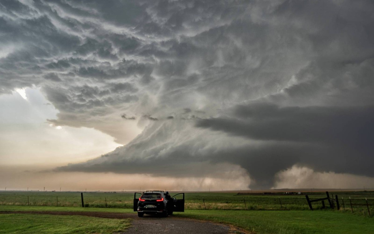 A storm chaser s vehicle parked on a dirt road observing a massive tornado forming under a dark, dramatic sky in an open field. Olustee, Oklahoma United States peja00028 Copyright: xConnectxImagesx