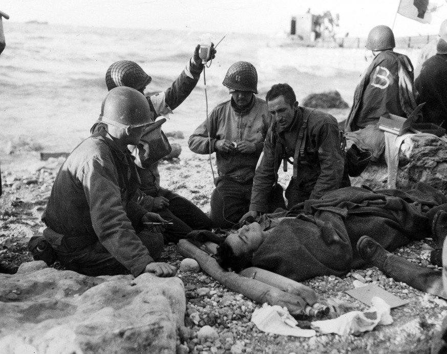 U.S. Army medical personnel administer a plasma transfusion to a wounded comrade, who survived when his landing craft went down off the coast of Normandy, France, in the early days of the Allied landi ...