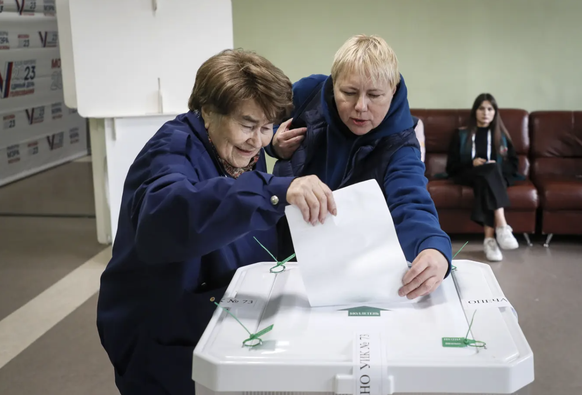 Einer Rentnerin wird in einem Moskauer Wahllokal beim Einwerfen des Stimmzettels geholfen.