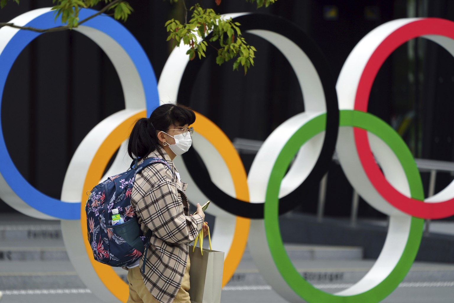 A woman wearing a protective mask to help curb the spread of the coronavirus walks in front of he Olympic Rings Tuesday, April 6, 2021, in Tokyo. The Japanese capital confirmed more than 390 new coron ...