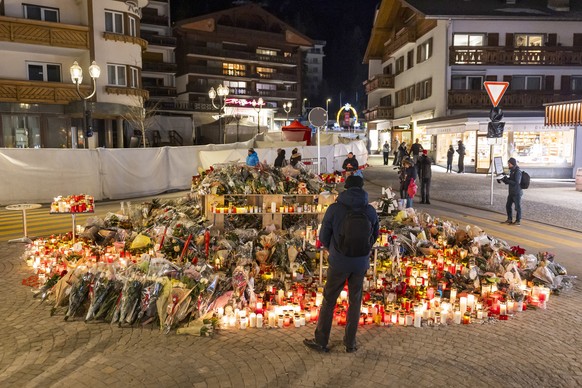 epa12629510 Flowers and candles are pictured in tribute to the victims after the fire at the 'Le Constellation' bar and lounge in Crans-Montana, Switzerland, 05 January 2026. At least 40 peo ...