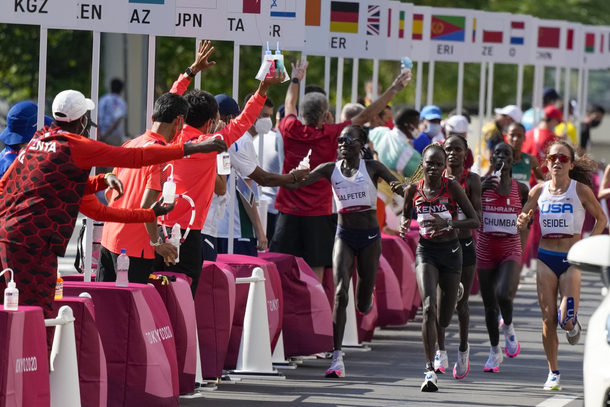 Runners pass a water station during the women's marathon at the 2020 Summer Olympics, Saturday, Aug. 7, 2021, in Sapporo, Japan (AP Photo/Shuji Kajiyama)