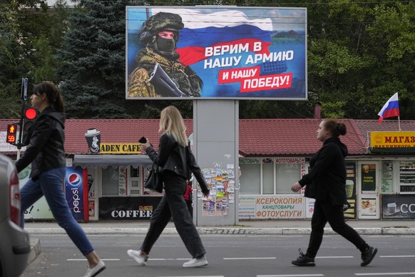 FILE - People walk past a billboard displaying a soldier and a Russian flag and reading &#039;We believe in our army and our victory&#039; in Luhansk, Luhansk People&#039;s Republic controlled by Russ ...