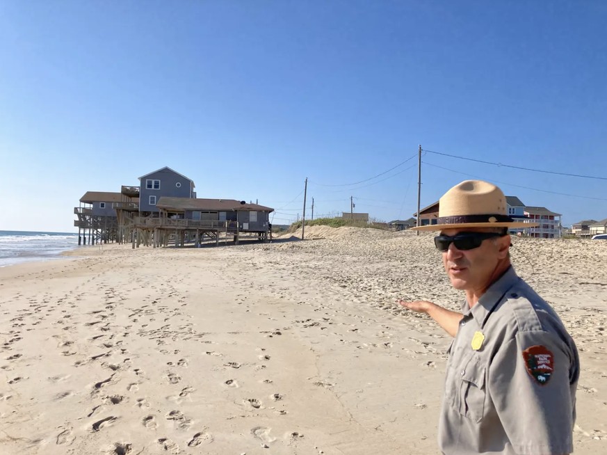 Dave Hallac, Superintendent des National Park Service, am Strand von Rodanthe (North Carolina). Im Hintergrund sind Ferienhäuser auf Stelzen zu sehen, die sich im Meer befinden.