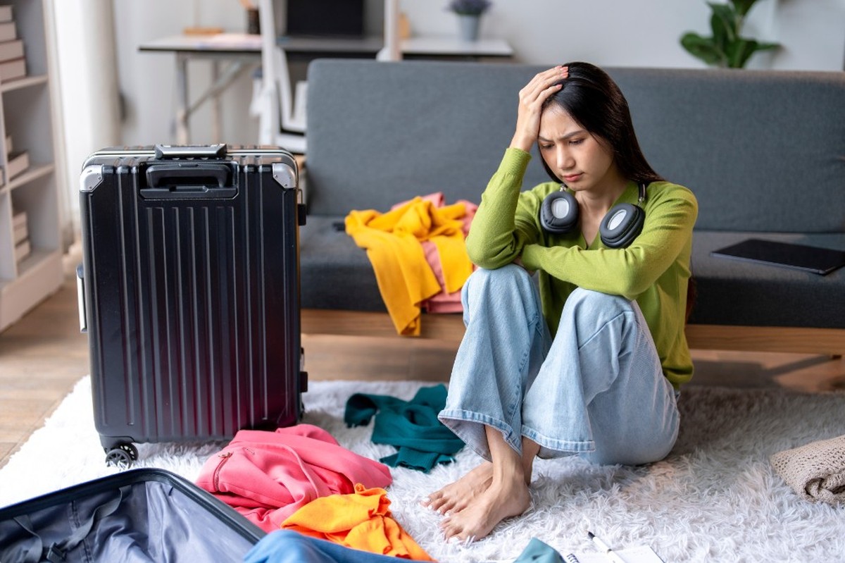 Young woman is sitting on the floor feeling stressed about packing her suitcase