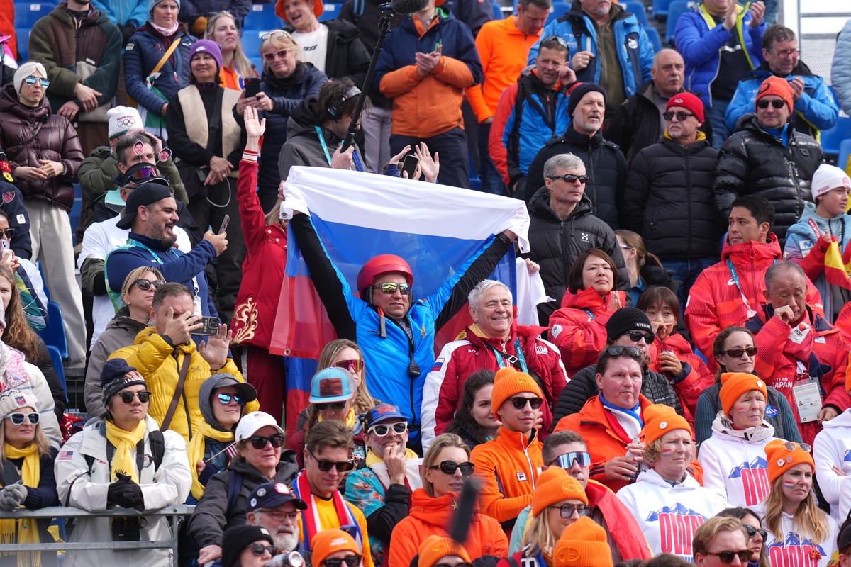 A fan holds up a Russian flag as Varvara Voronchikhina, of Russia, climbs on the podium to receive her gold medal for the alpine skiing women's super-G standing at the 2026 Winter Paralympics, in ...