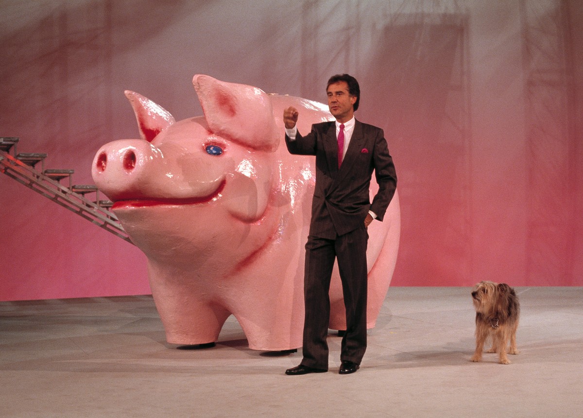 Der Schweizer Fernseh-Moderator Kurt Felix und sein Hund Sheriff vor einem riesigen Sparschwein waehrend einer Probe fuer die TV-Sendung "Supertreffer", aufgenommen 1987 in Flims, Graubuende ...