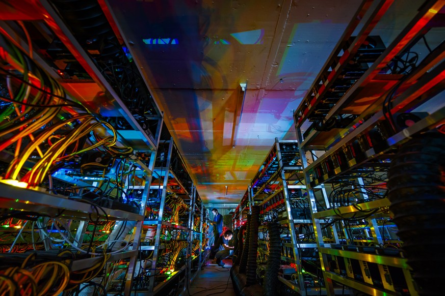 Alpine Mining employees Bertrand Deldon, left, and Patrick Widmer, right, are lit by the LED status lights of electronic boards during a long exposure photograph at a cryptocurrency mine in the small  ...