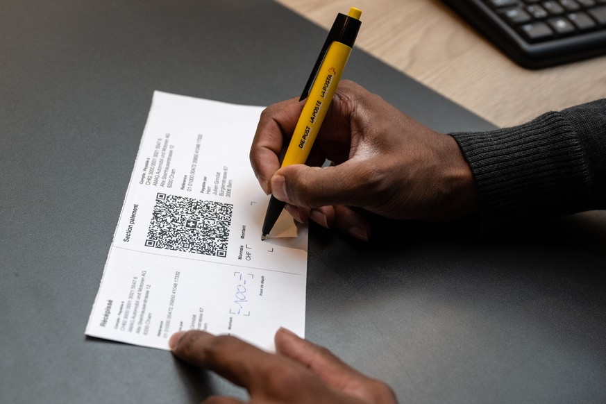 Ein Mitarbeiter der Post fuellt einen Einzahlungsschein mit QR Code aus, am Mittwoch, 28. September 2022, in einer Postfiliale in Bern. Die rosa und orangen Einzahlungsscheine werden per 1. Oktober mi ...