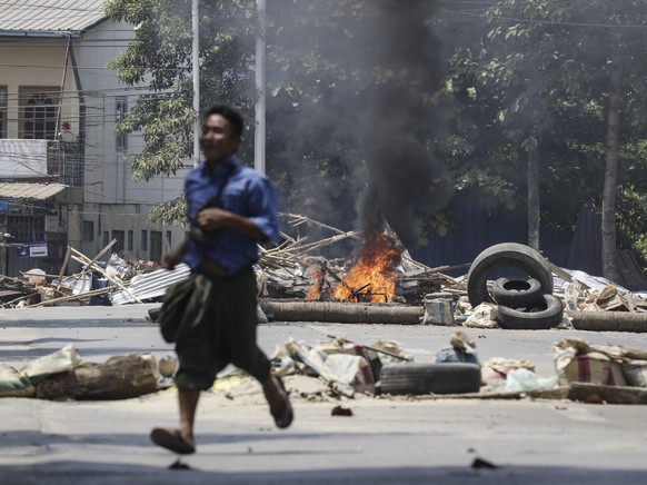 epa09711494 (19/31) (FILE) - A man runs past a burning a roadblock set on fire by military personnel at a railway staff compound during a raid in Yangon, Myanmar, 10 March 2021 (reissued 27 January 20 ...