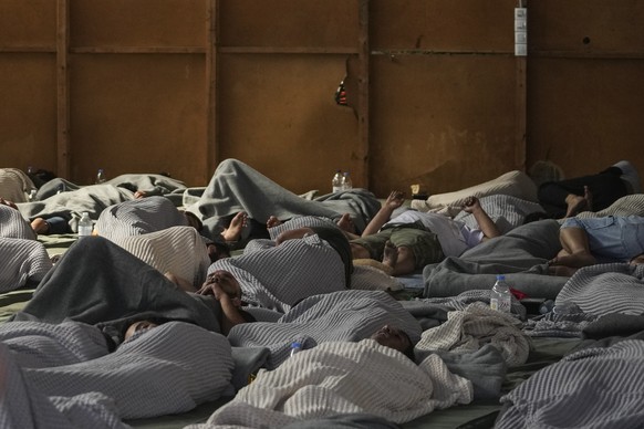 Survivors of a shipwreck sleep at a warehouse at the port in Kalamata town, about 240 kilometers (150 miles) southwest of Athens, Wednesday, June 14, 2023. A fishing boat carrying migrants capsized an ...