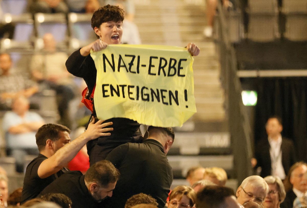 epa10714875 Security remove a protester holding a banner reading "Expropriate Nazi heir" during the annual general meeting of Porsche Automobile AG in Stuttgart, Germany, 28 June 2023. EPA/R ...