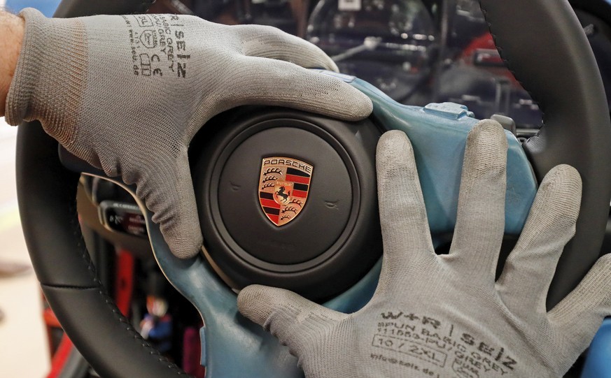 epa07380434 An employee wearing gloves checks a Porsche sign at a production station of sports cars at the German car manufacturer Porsche in Stuttgart, Germany, 19 February 2019. Porsche AG is a list ...