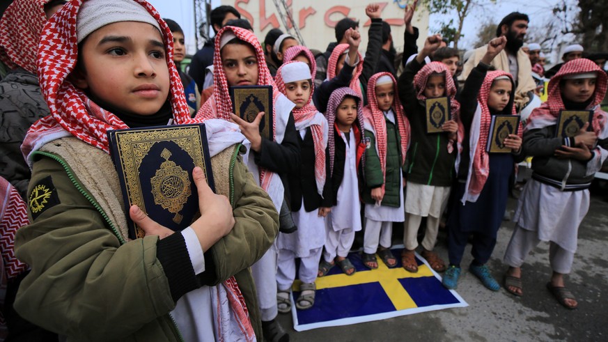 epa10426784 Supporters of Pakistan Markazi Muslim League party holds copies of the Koran as they stand on a Swedish flag, during a protest against Sweden, in Peshawar, Pakistan, 24 January 2023. Pakis ...