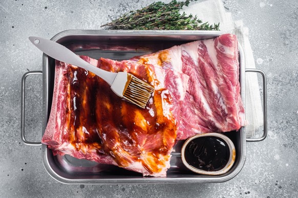 Cooking of Raw pork spare ribs with barbecue sauce. Gray background. Top view.