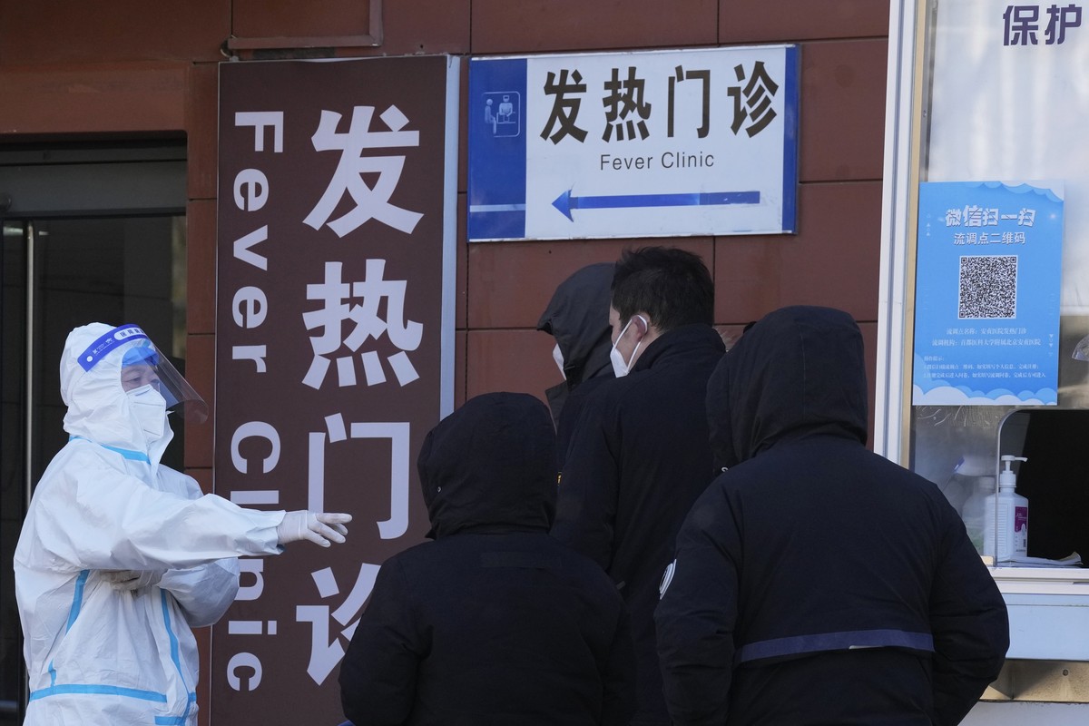 A worker in protective overalls controls the line outside the fever clinic at a hospital in Beijing, Saturday, Dec. 10, 2022. A rash of COVID-19 cases in schools and businesses were reported Friday in ...
