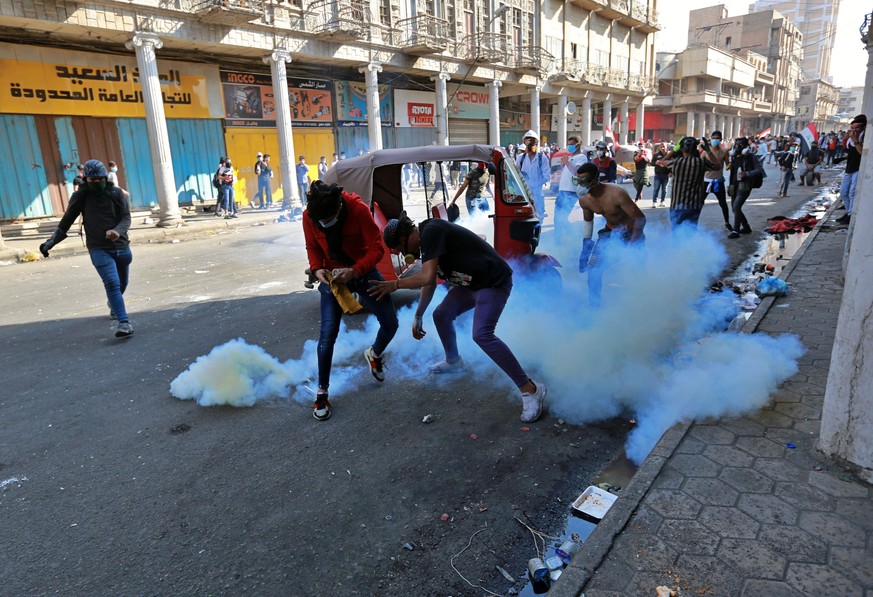 Anti-government demonstrators react to tear gas fired by Iraqi riot police during clashes in al-Rashid Street, Baghdad, Iraq, Sunday, Nov. 17, 2019. (AP Photo/Hadi Mizban)