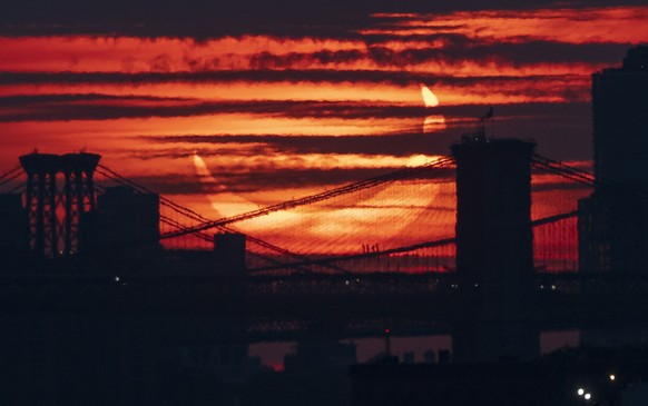 epa09259321 A partial solar eclipse rises over bridges crossing the East River in New York, New York, USA, 10 June 2021. A partial solar eclipse occurs when a portion of the Earth is engulfed by the s ...